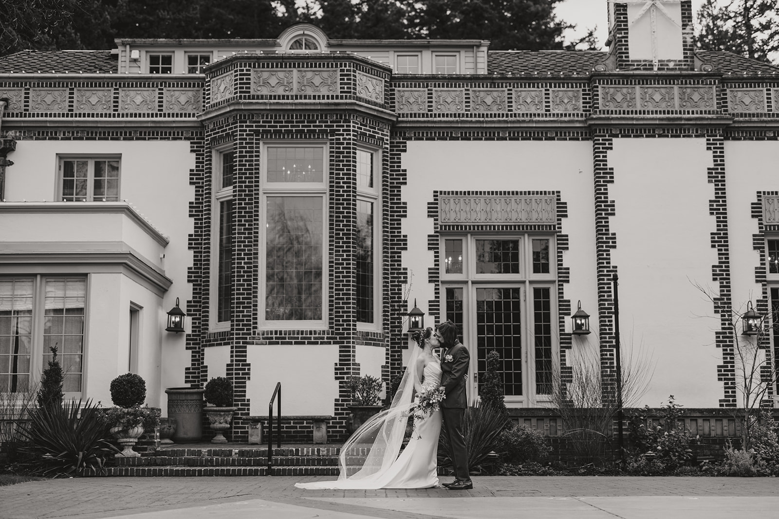 Bride and groom sharing a kiss at a manor house, black and white photograph with purple duotone overlay